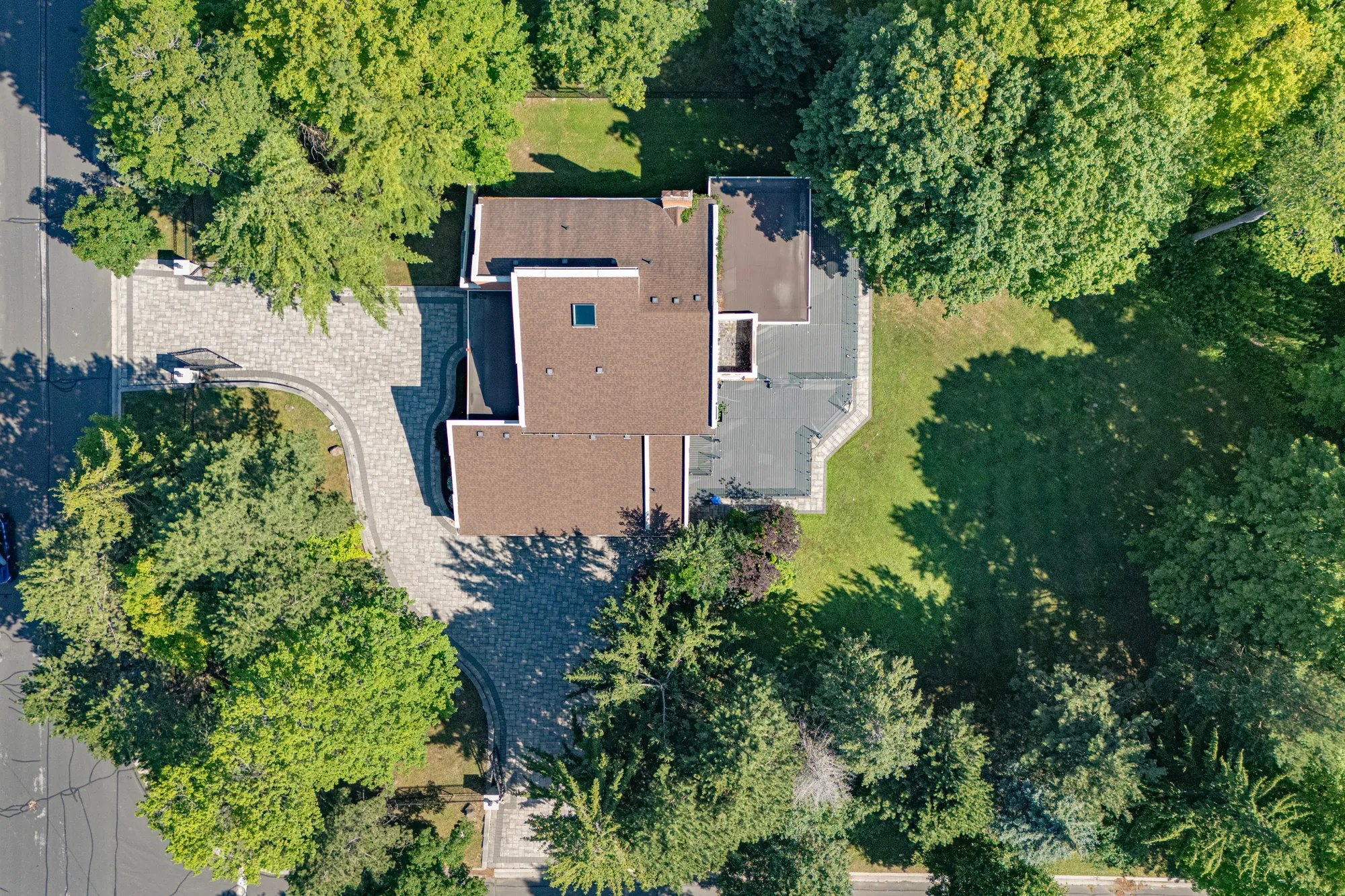 Straight down on the house: brown and flat grey roofs, the paved drive from the street at the left, the lawn and trees around it