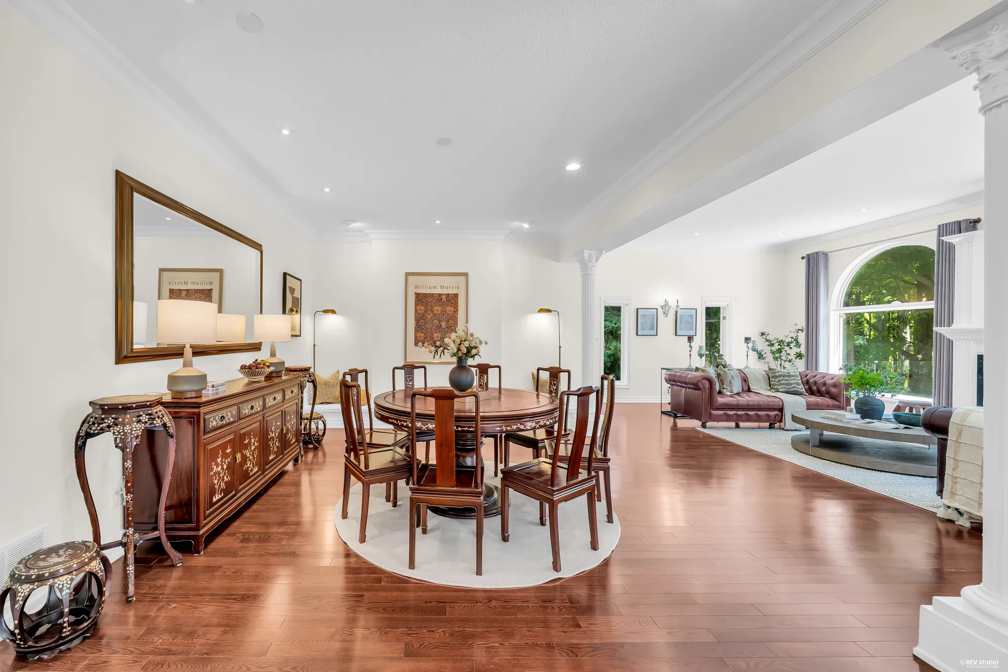 The round table and carved chairs, an inlaid sideboard under a large mirror, the family room&rsquo;s sofas at the right