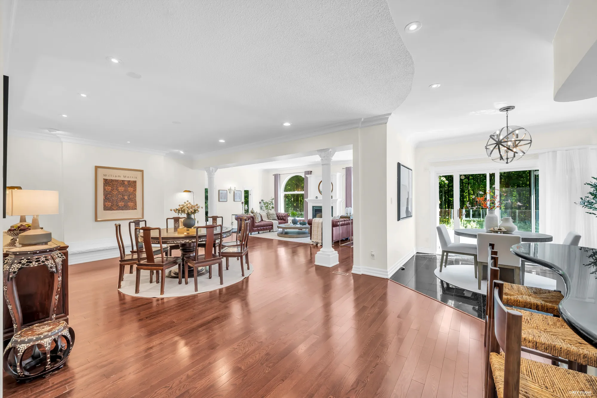 The dining area from the kitchen side: the round table, an inlaid side table, the family room and its arched windows beyond, the breakfast nook at the right
