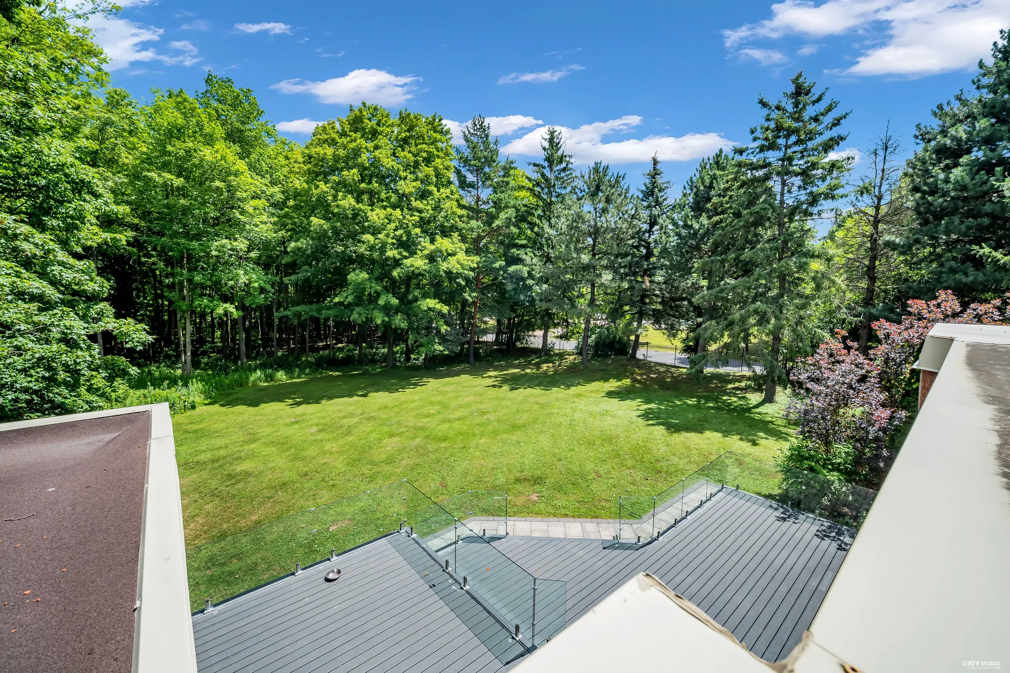 From the balcony: the roofs below, the deck and its glass railing, the lawn and tall trees
