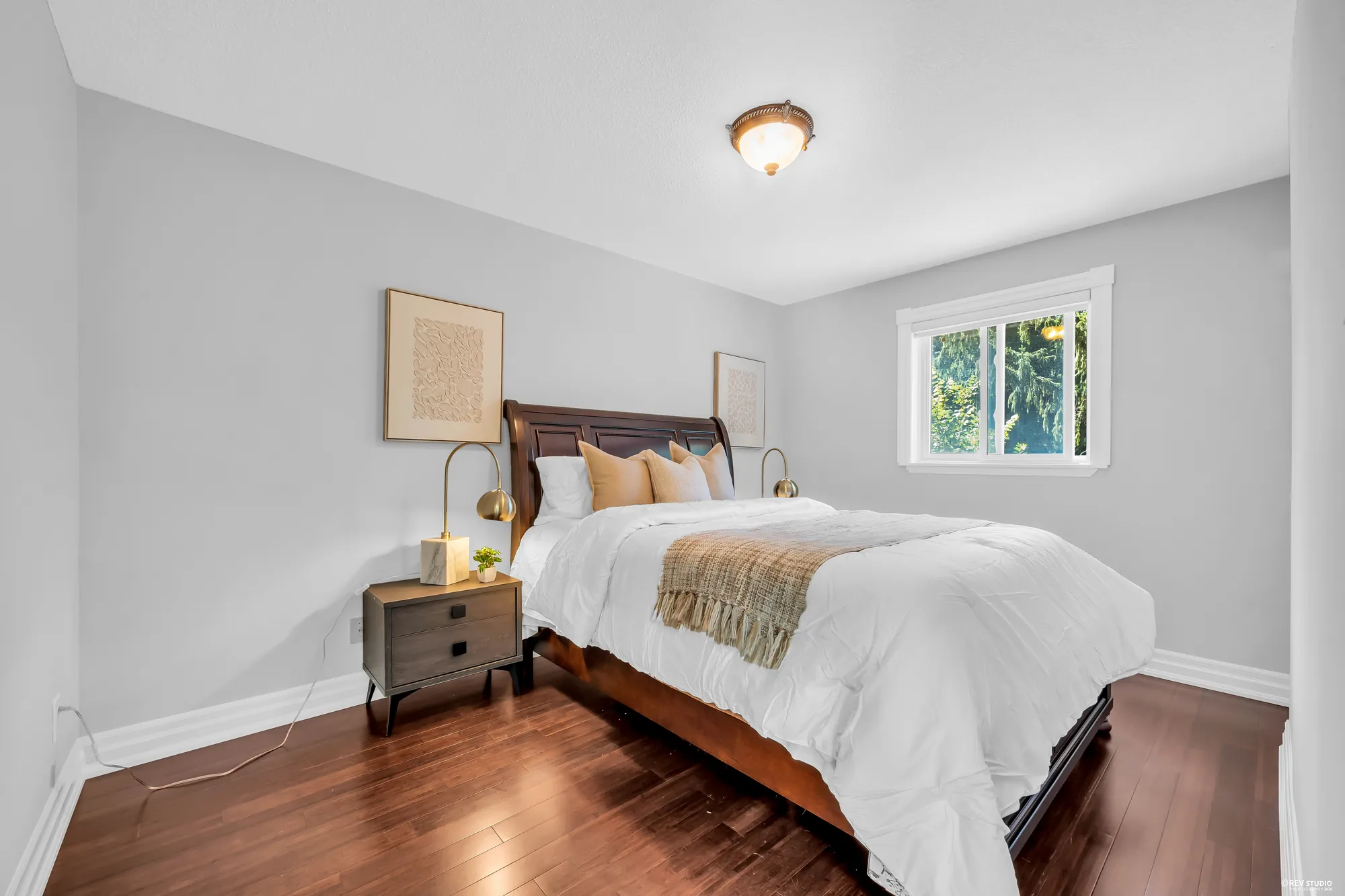 A bedroom with grey walls: a wood sleigh bed, a night table with a brass lamp, a window onto the trees