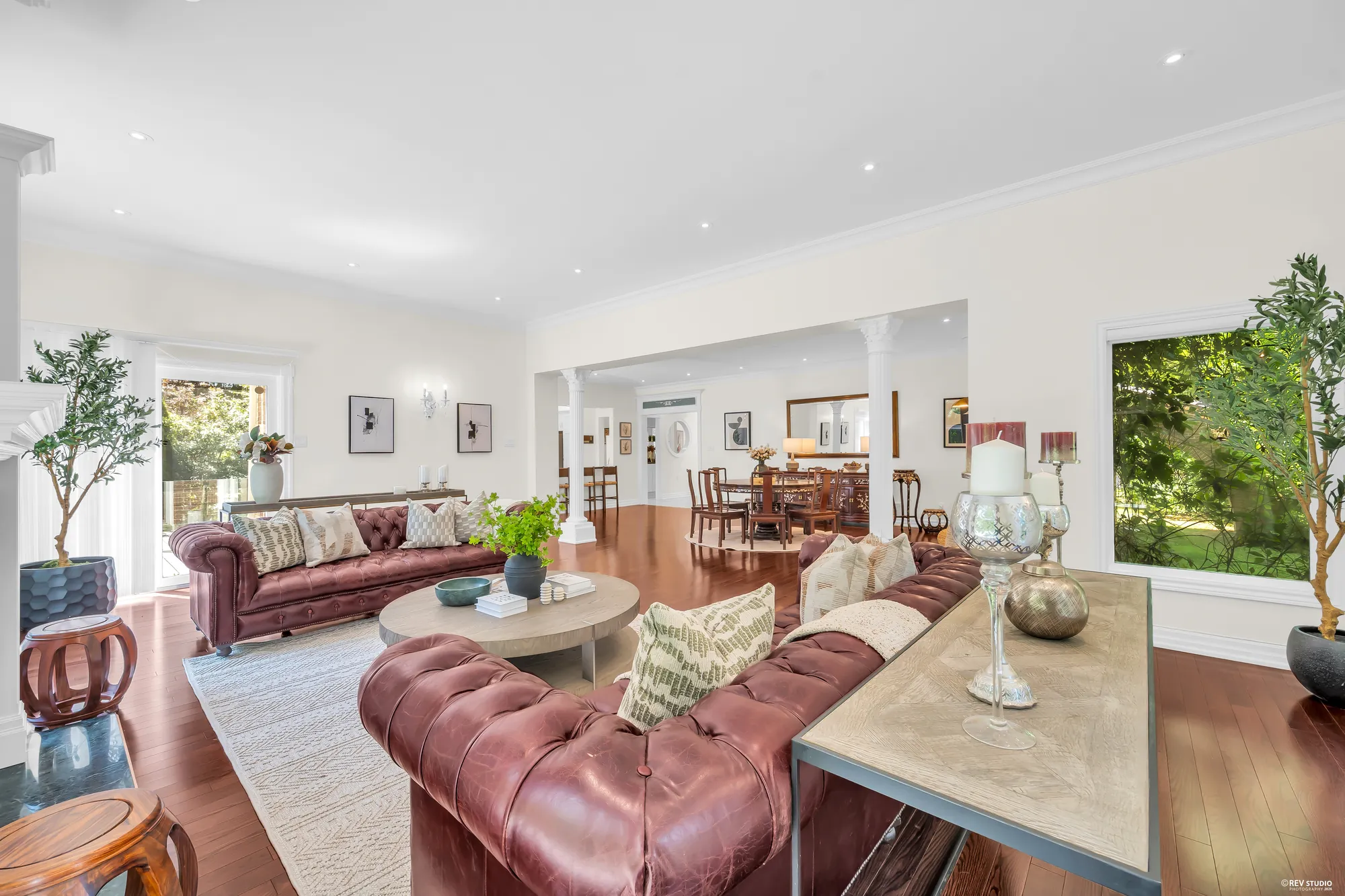 From the family room toward the dining area between white columns, the kitchen beyond, a large window onto the trees at the right