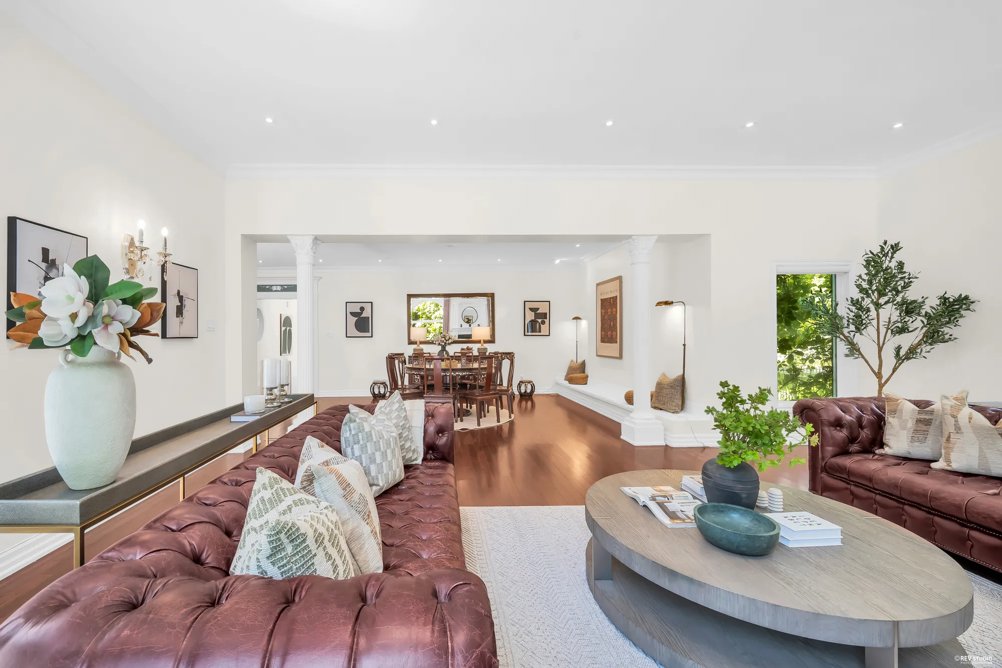 A leather sofa and an oval coffee table in the foreground, the round dining table through the columns beyond
