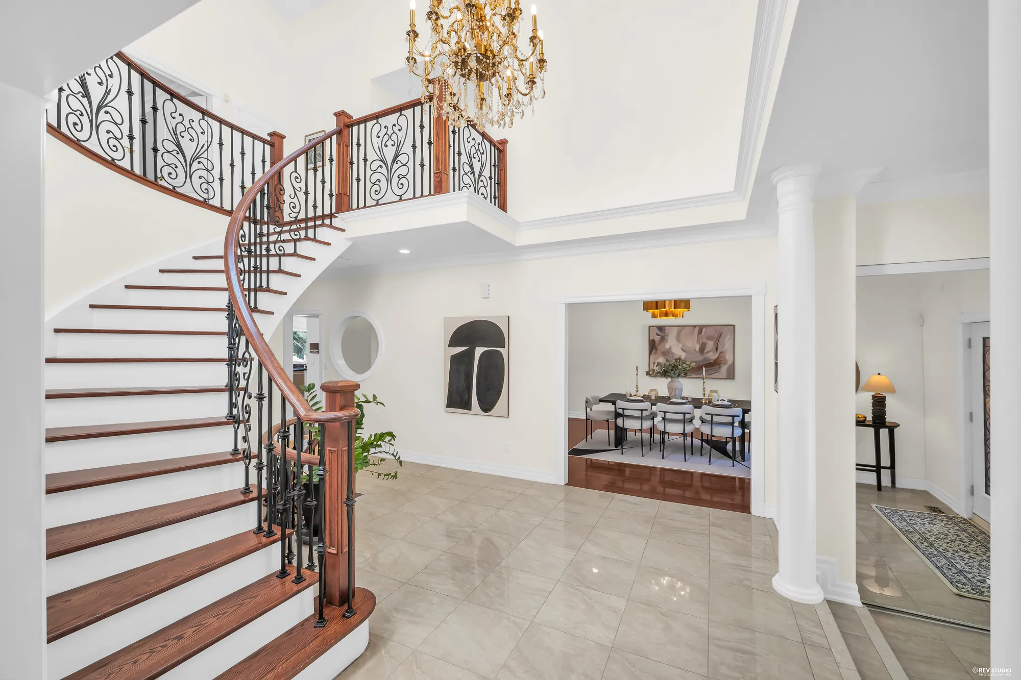 The curved stair from the foyer, the front dining room through an opening at the right with its table and chairs