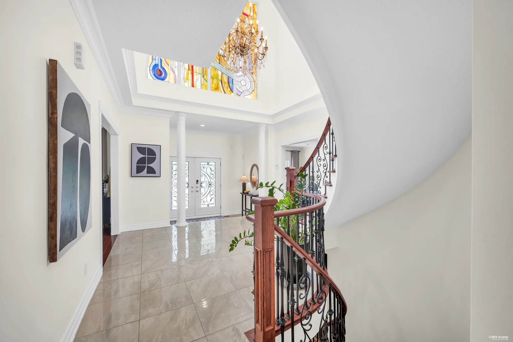 The foyer from the hall: the front doors and the columns, the stained-glass window high above, the stair rail at the right