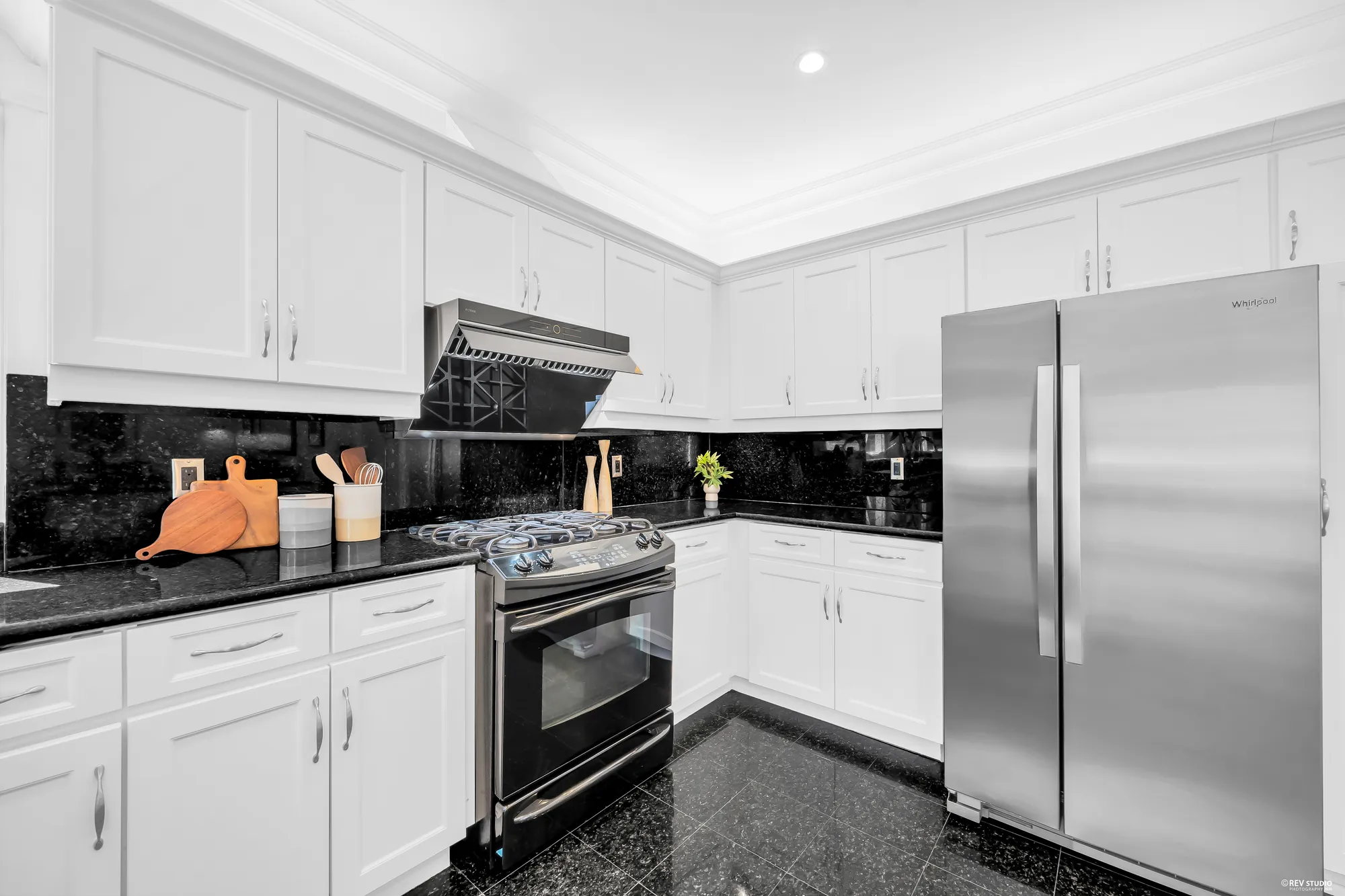 The kitchen: white cabinets, black granite counters and backsplash, a stainless range under a hood, a stainless refrigerator