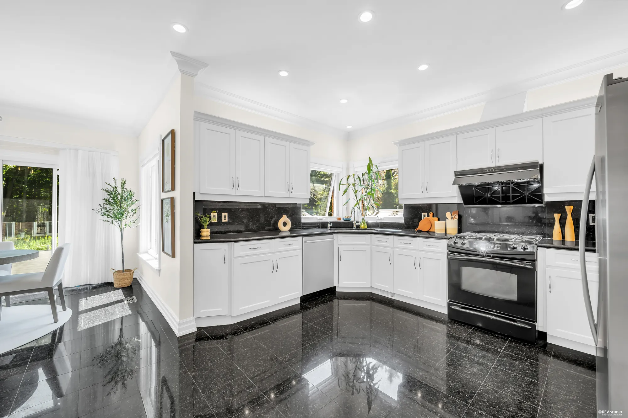 The kitchen from the nook: white cabinets on two walls, black granite counters, the range under its hood, a black granite floor