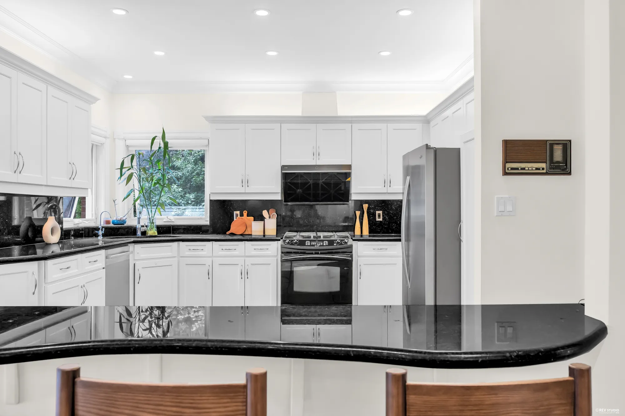 White cabinets, a window over the sink, the range and the refrigerator, the curved bar with two stools in the foreground