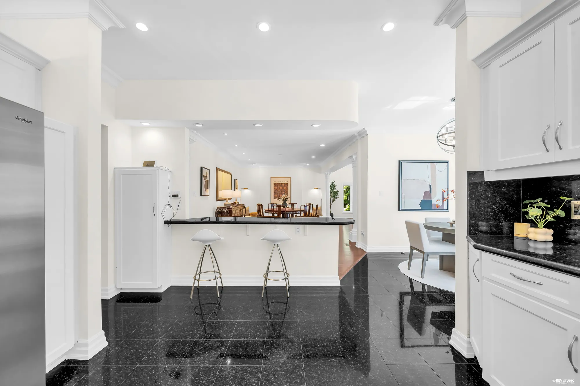 From the kitchen toward the dining area: a counter with two bar stools, the round table beyond, a black granite floor