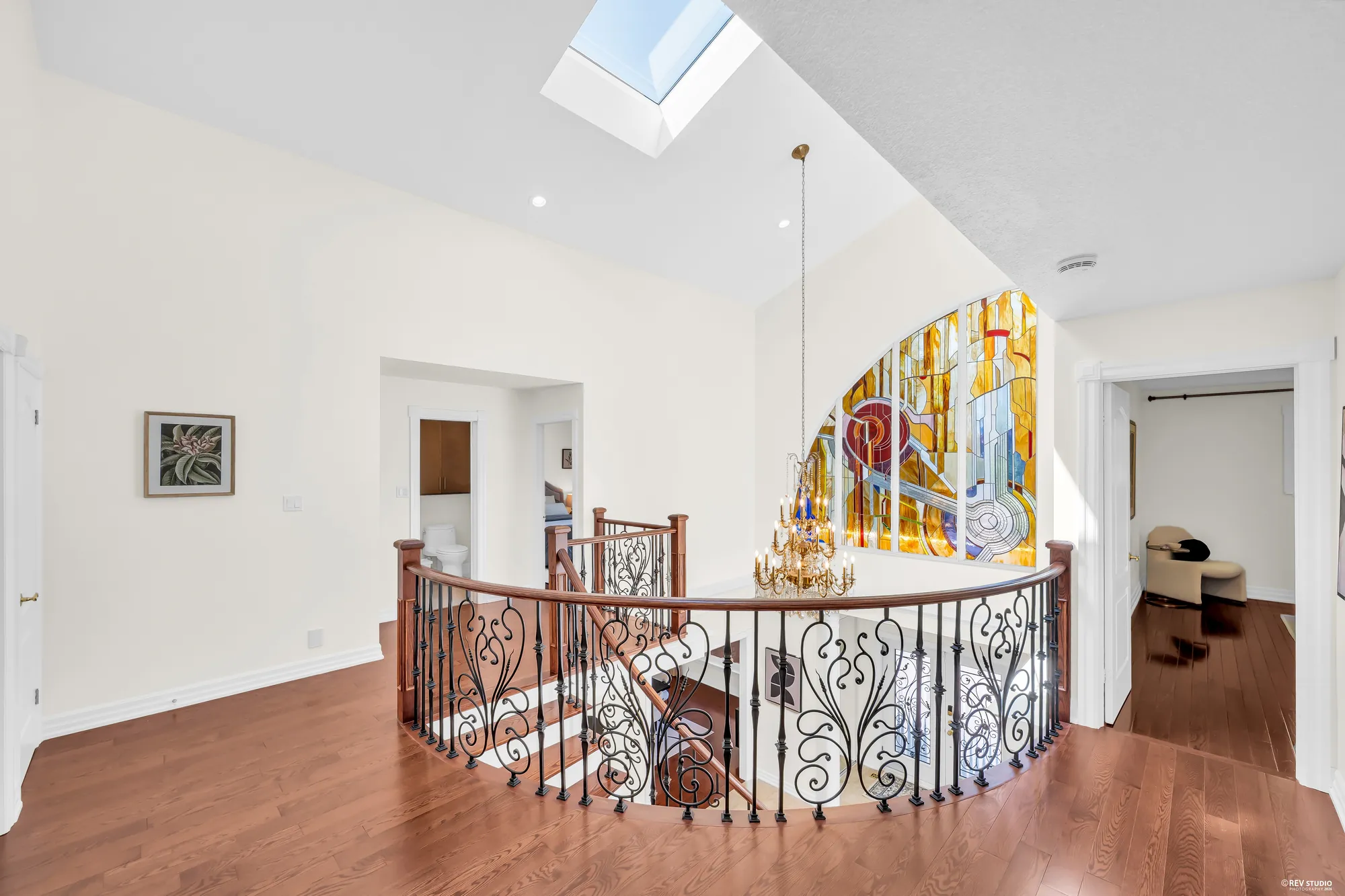 The landing around the open stairwell, the stained-glass window and the chandelier, doorways to a bathroom and the bedrooms
