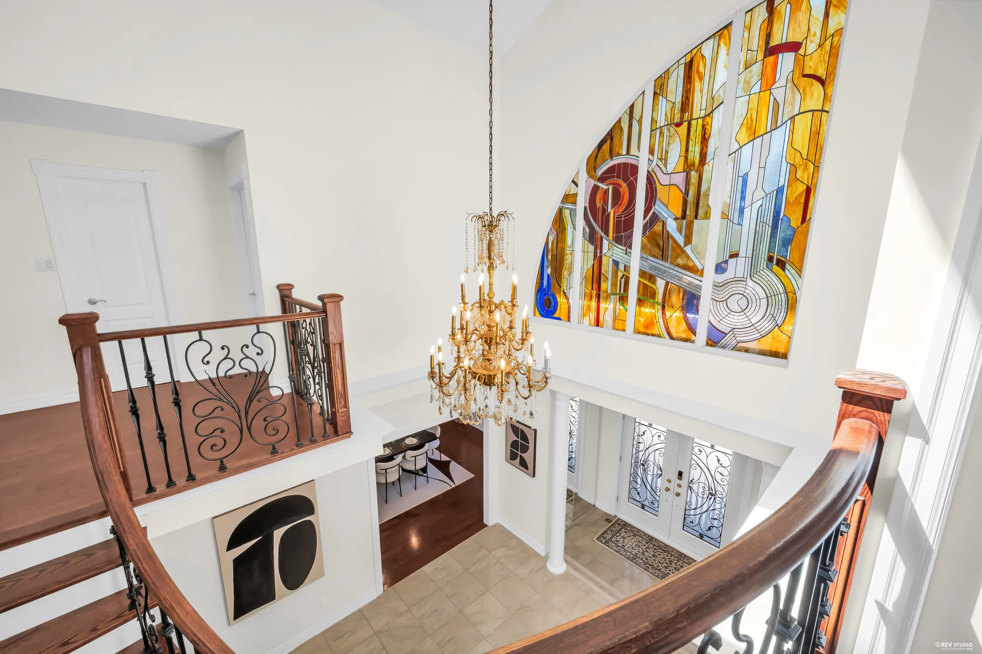 Looking down from the landing into the foyer: the stained-glass window, the chandelier, the front doors below