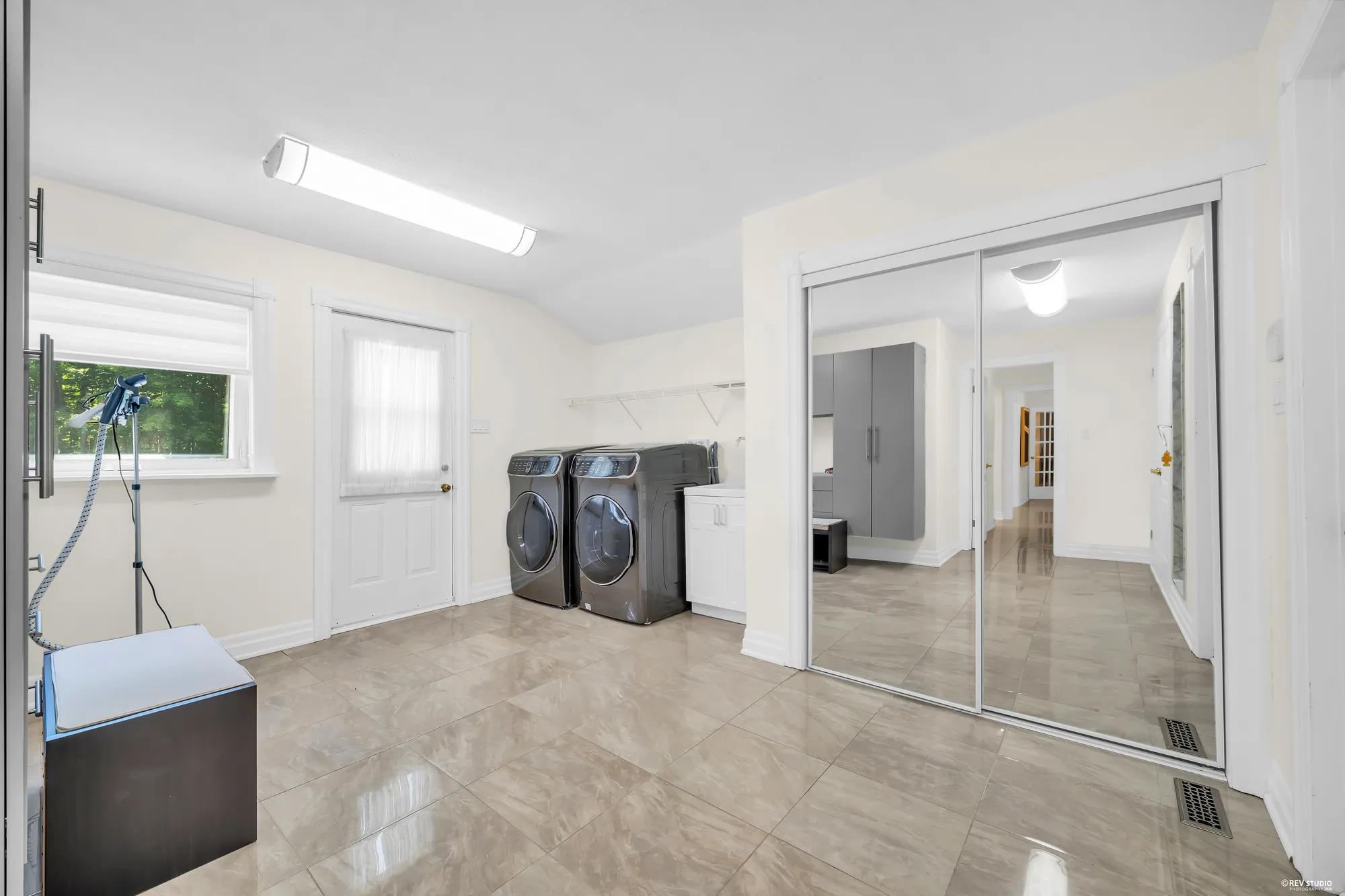 The laundry: a front-loading washer and dryer, a door with a window, a mirrored closet, a tiled floor