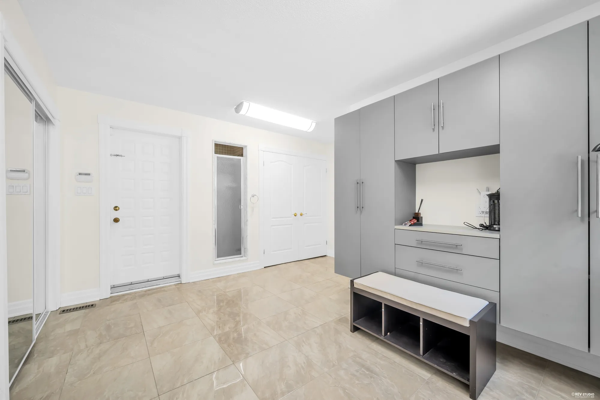 Grey built-in cabinets and a bench, white doors, a tiled floor
