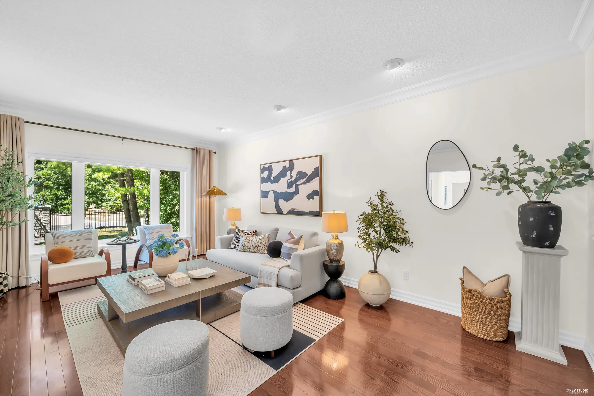 The living room toward its front window: sofas and armchairs, an olive tree, a round mirror and an abstract print