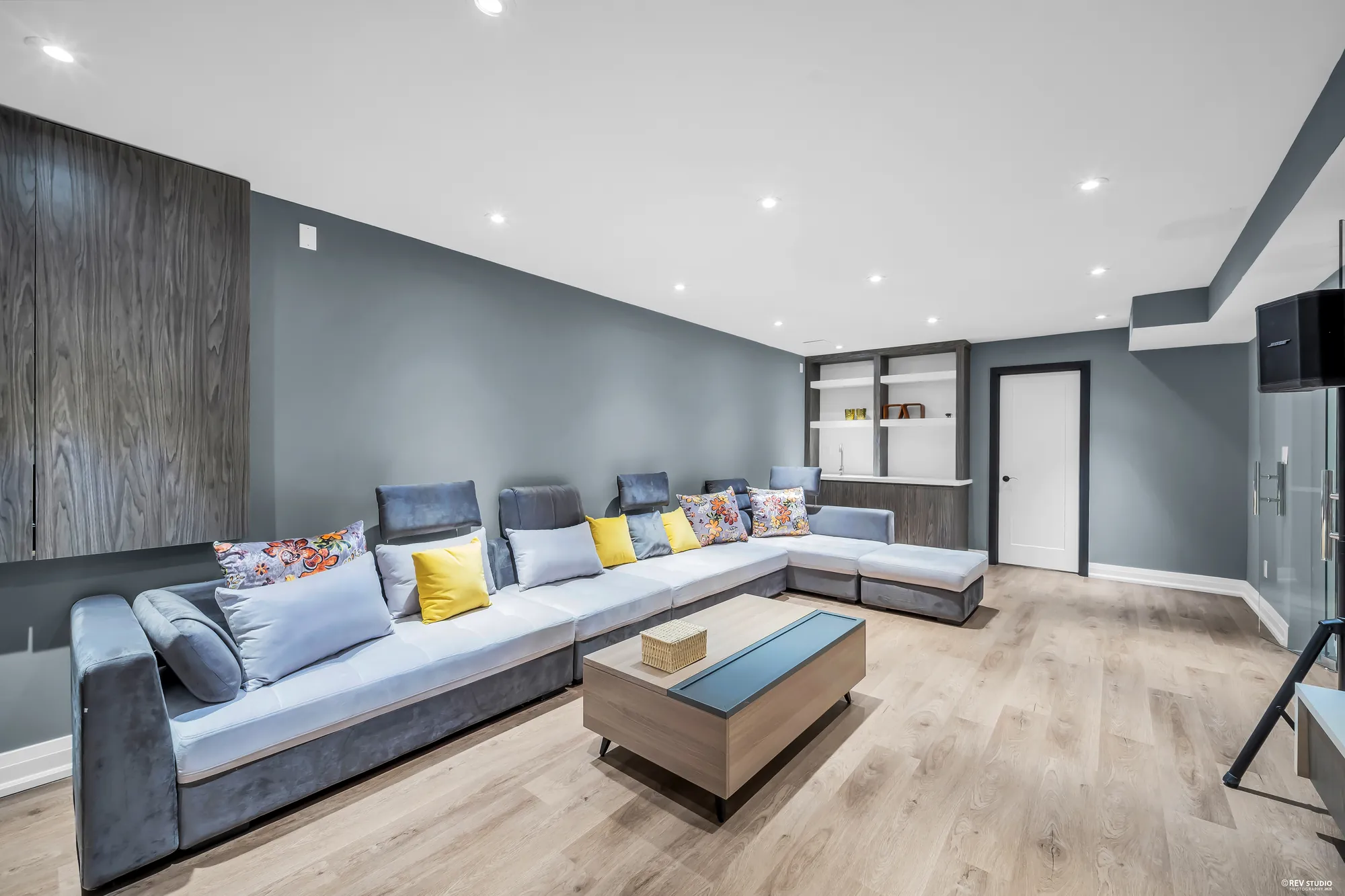 The sectional and a coffee table, built-in shelves, grey walls, a door at the back