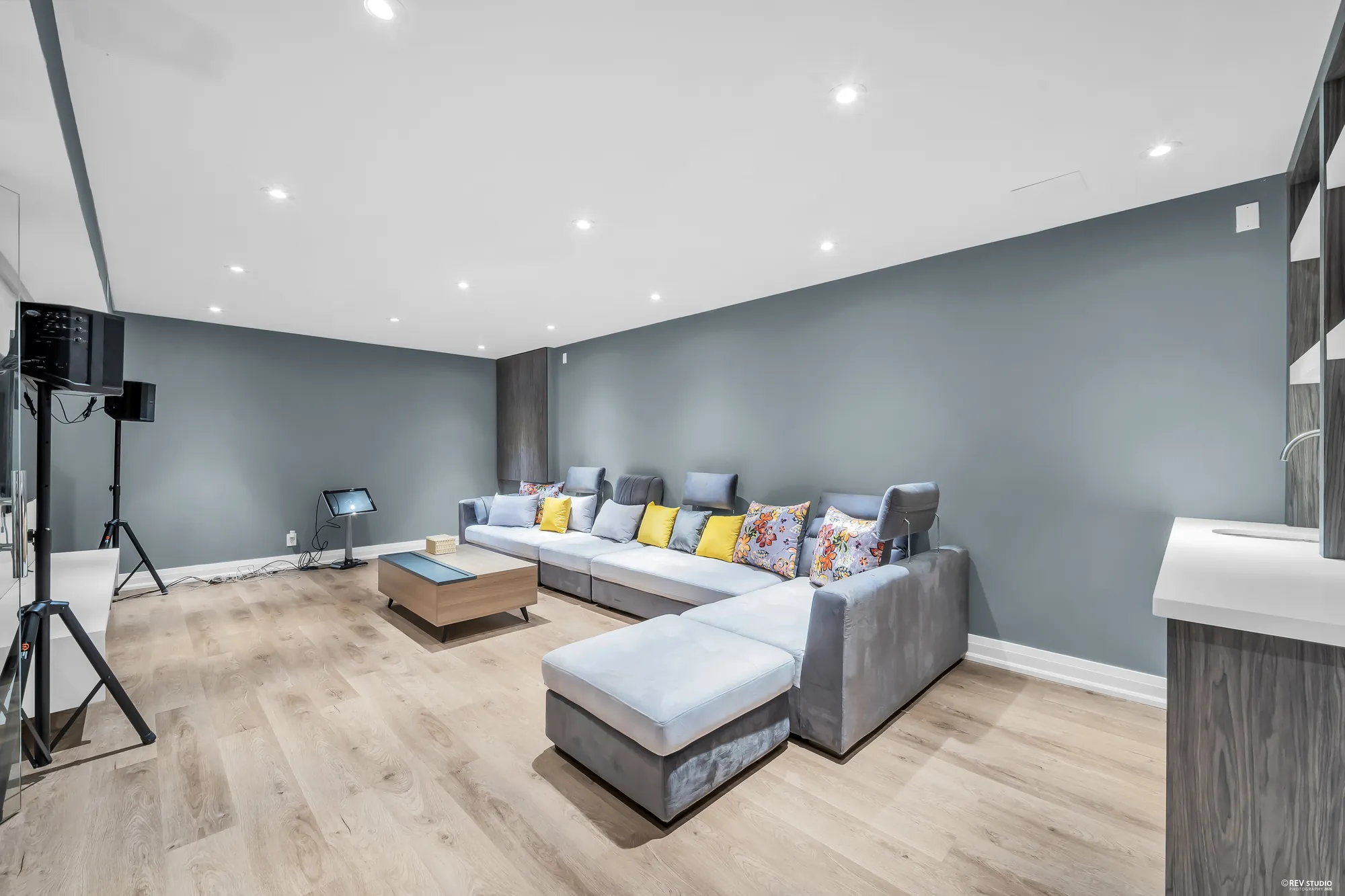The theatre room from the other end: the sectional, grey walls, speakers on stands, a counter at the right
