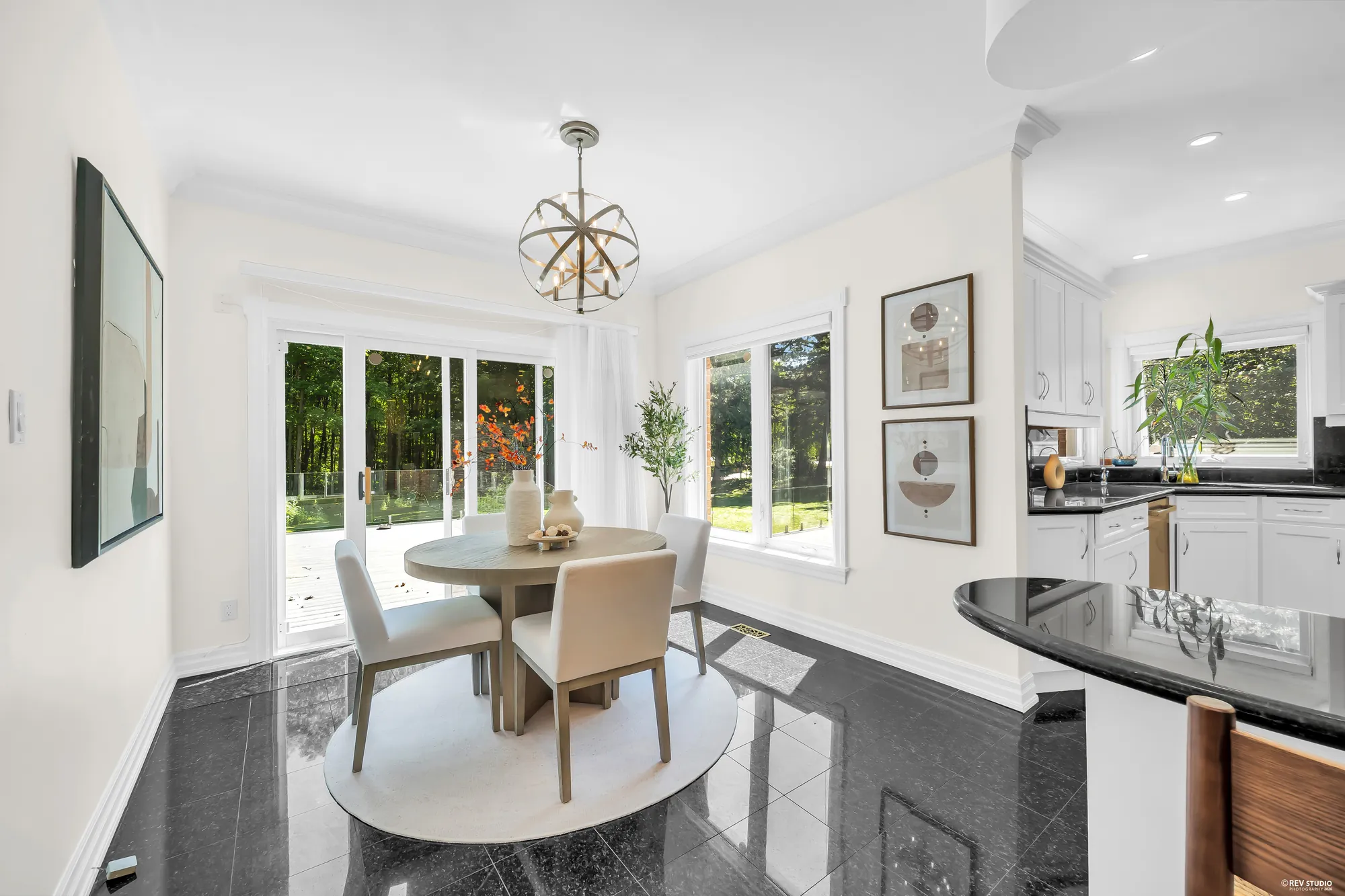 The breakfast nook: a round table with four chairs on a round rug, a black granite floor, sliding doors to the deck, a window onto the trees