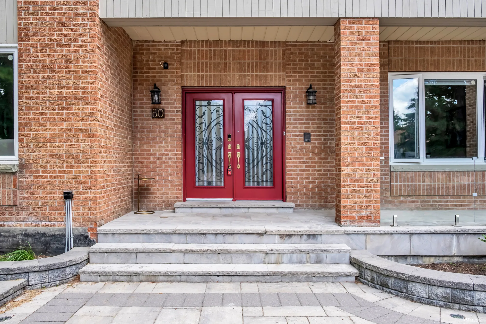 The covered entry: a red double door with iron scrollwork over the glass, black lanterns on the brick, the house number 50, wide stone steps