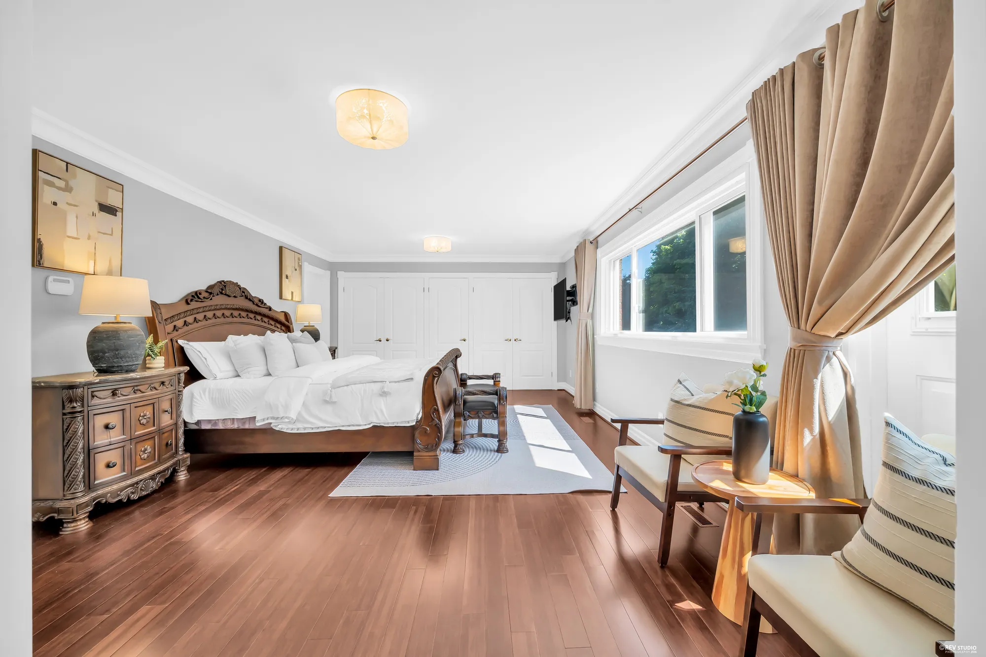The bed from the side, closets along the far wall, a window with tan curtains, an armchair
