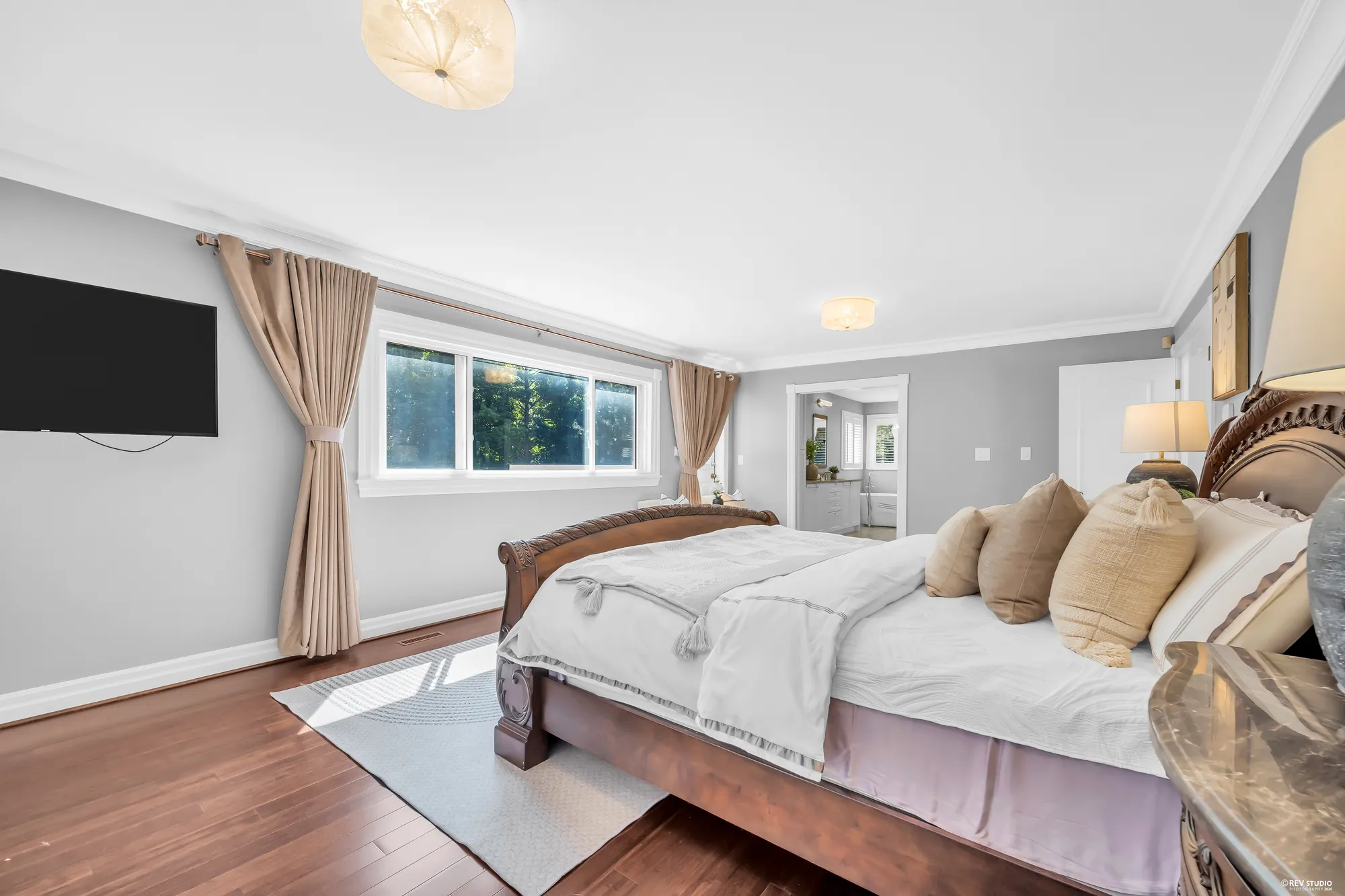 The bed, a television on the wall, the window, a doorway at the far end