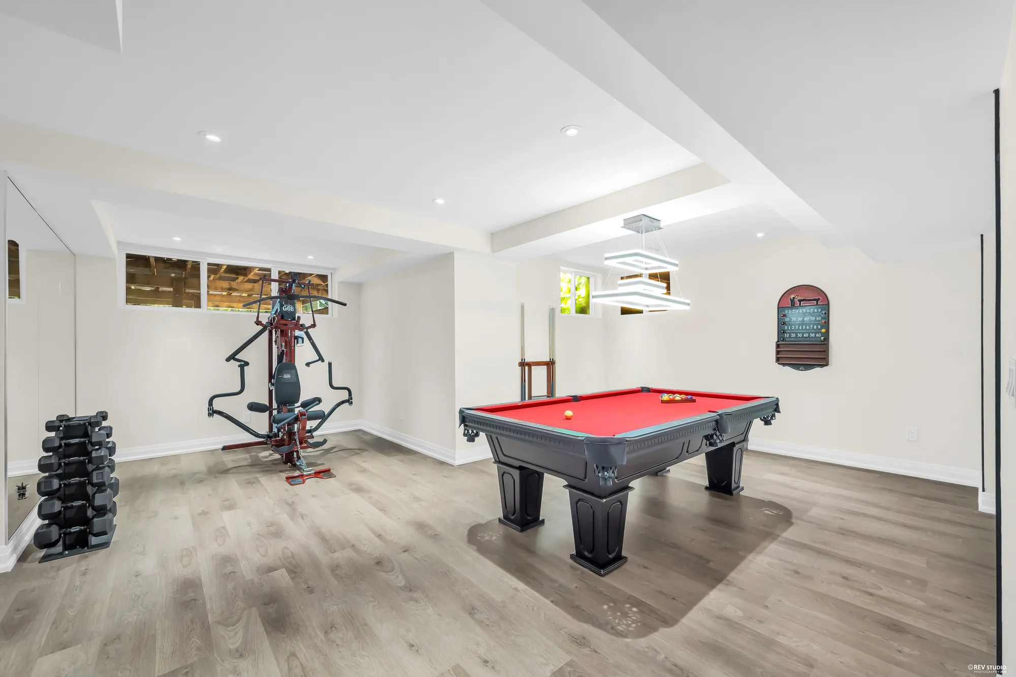 The recreation room: a pool table with red felt, a weight machine and dumbbells, small windows high in the wall