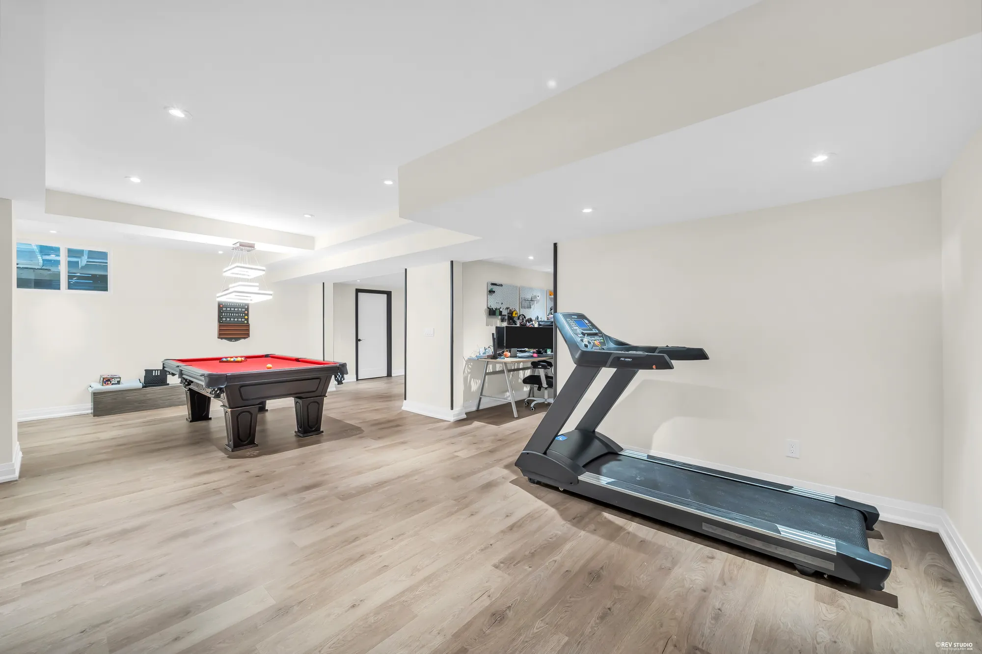 The recreation room toward its windows: the pool table, a treadmill, a desk at the far end